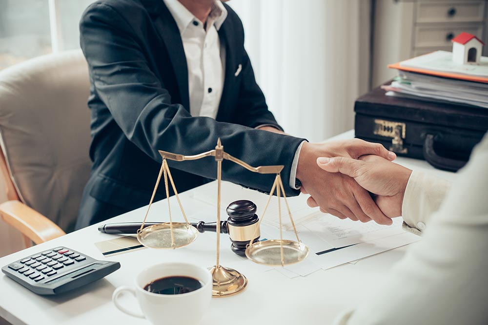 Deux personnes qui se serrent la main avec en premier plan un marteau de juge et une balance