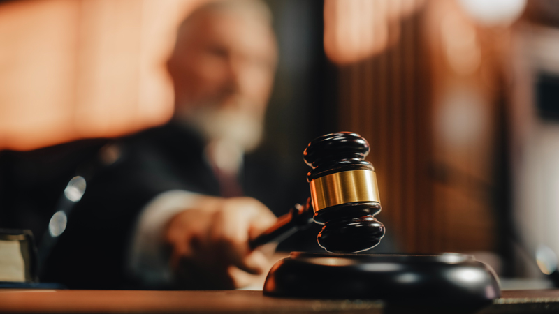 Un homme en fond en train de taper sur un support avec un marteau de juge